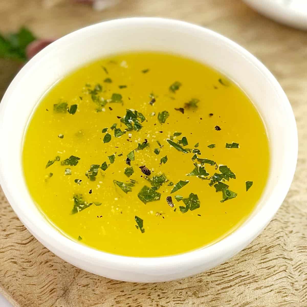 melted butter sauce in a white bowl on a wooden board sprinkled with parsley.