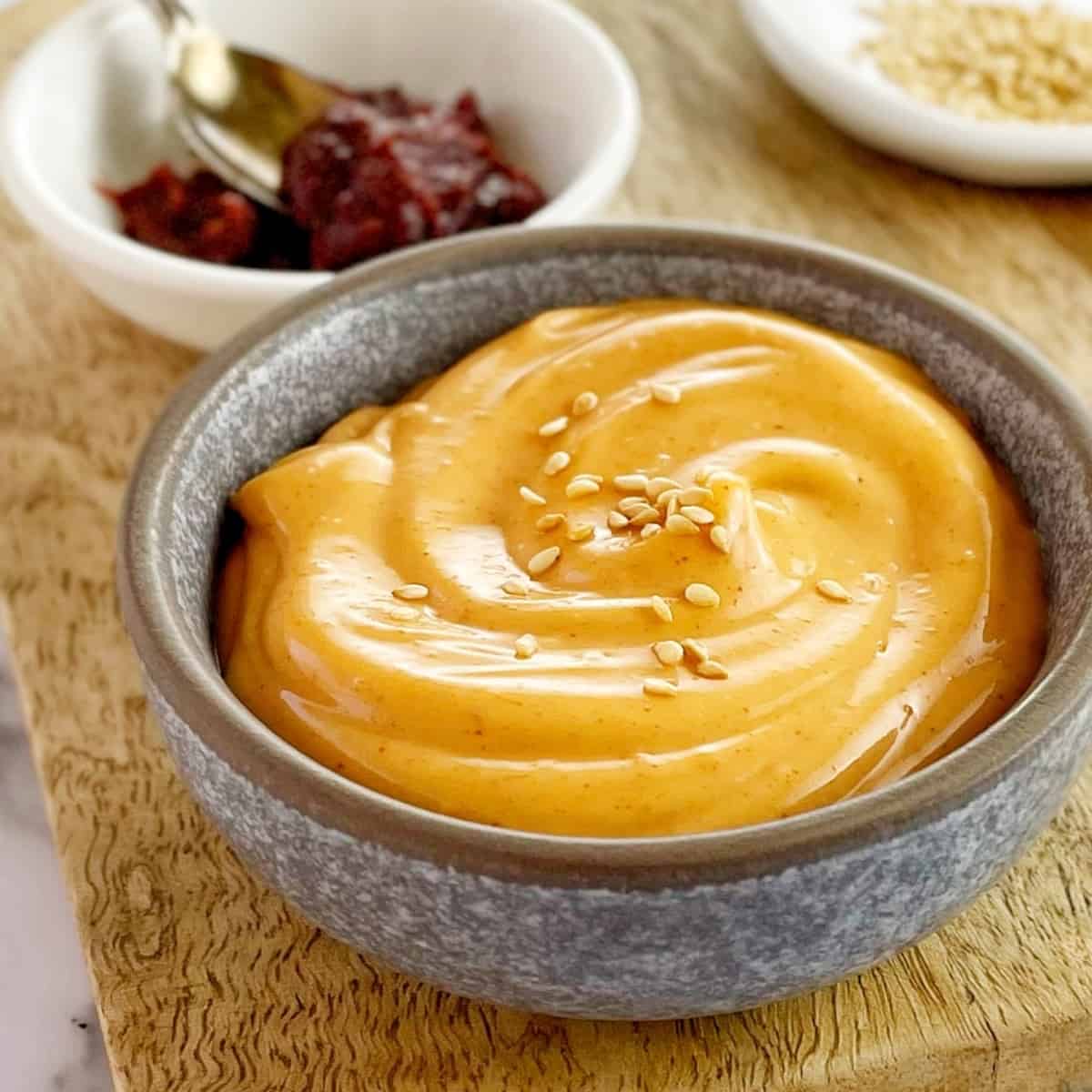 orange coloured mayonnnaise in a grey bowl on a wooden board.