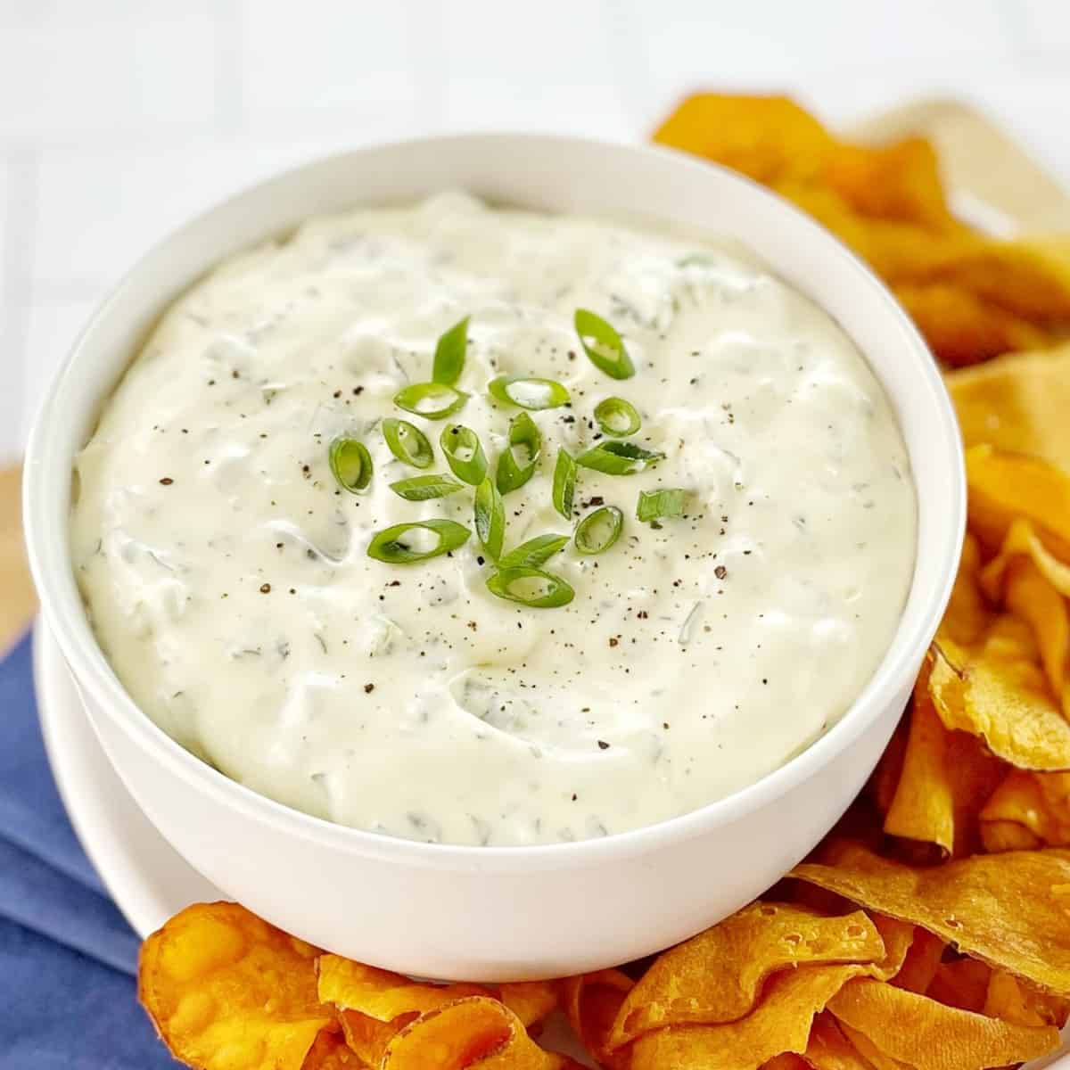 creamy green onion dip in a white bowl with sliced green onions on top with sweet potato chips on the side.
