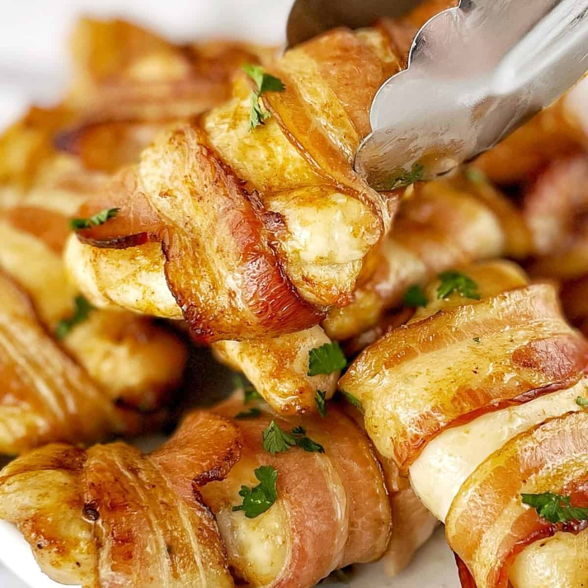 baked chicken thighs wrapped in slices of bacon with one piece being held by tongs.