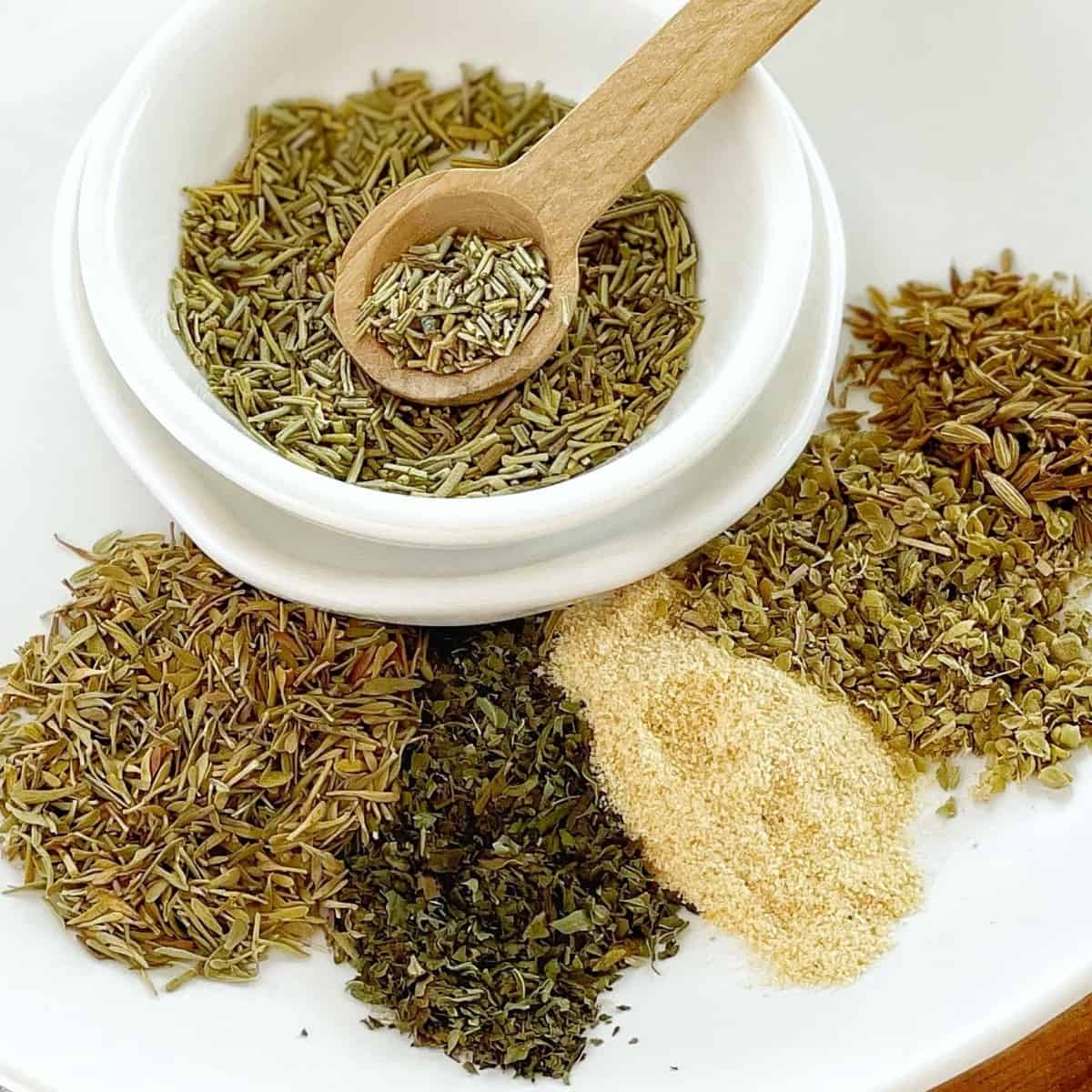 small piles of dried herbs on a white plate with a small wooden spoon.