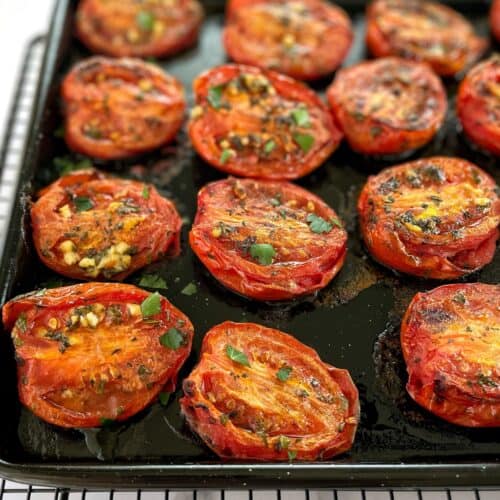 cooked tomato halves in a black baking tray sprinkled with garlic and herbs.