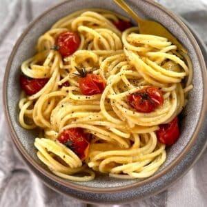 spaghetti pasta with cherry tomatoes in a gray bowl with a fork.
