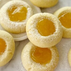 cookies with yellow lemon curd in the center on a white benchtop dusted with icing sugar.