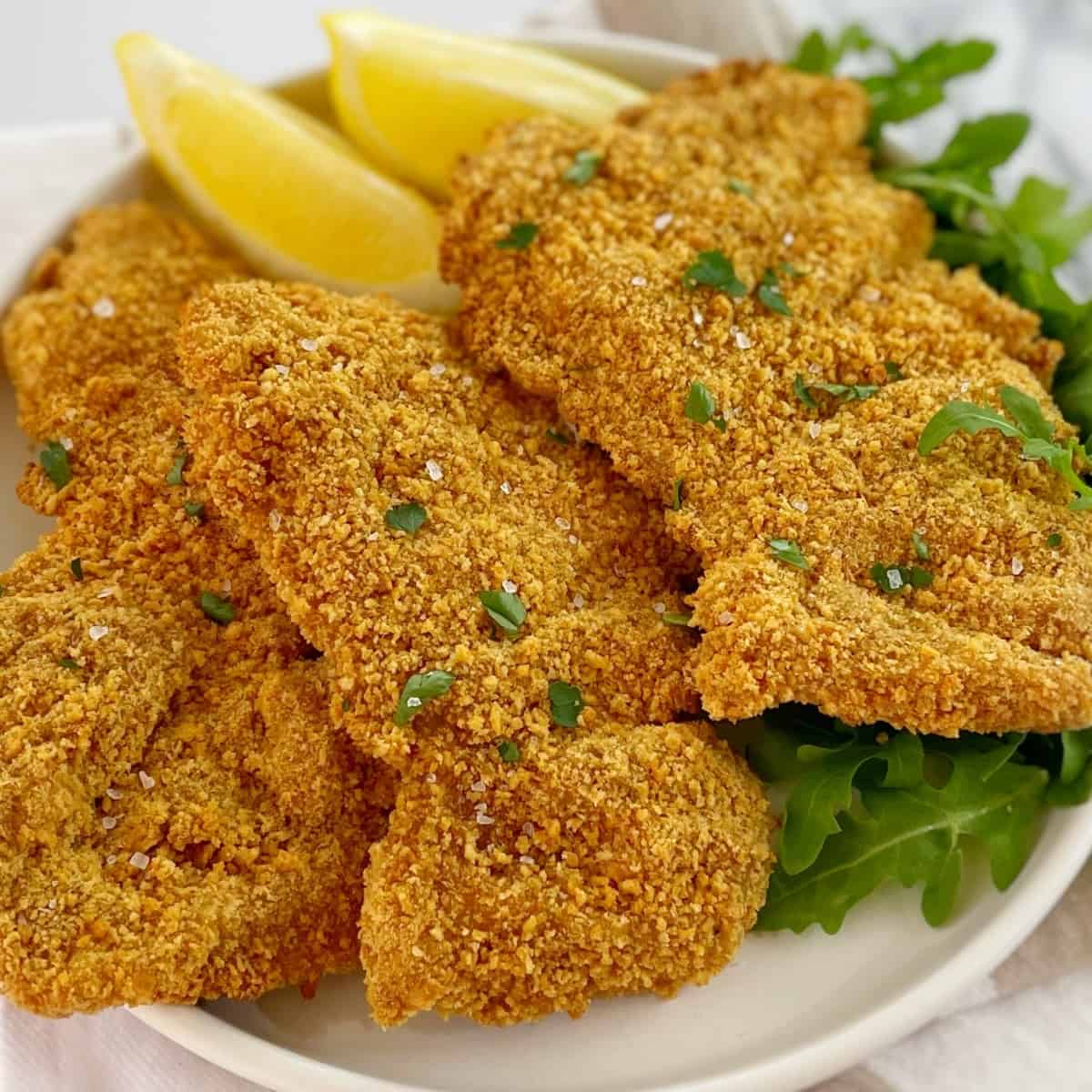 crumbed chicken thighs on a white plate with green lettuce and lemon wedges.