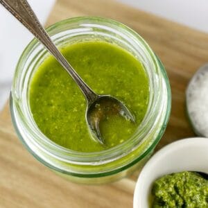 green salad dressing in a glass jar with a spoon on a wooden board.