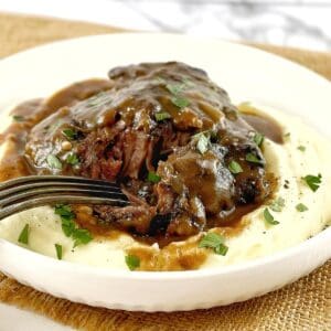 beef cheeks with sauce on a bed of mashed potato in a white bowl with a fork.