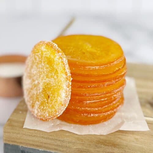 Slices of candied orange sitting on a wooden board.