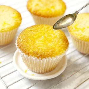Lemon cupcakes sitting on a wire rack with a spoon.