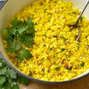 Yellow rice in a blue pot with parsley and a spoon.