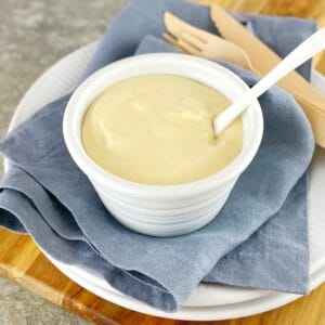 creamy sauce in a white bowl on wooden board with a spoon.