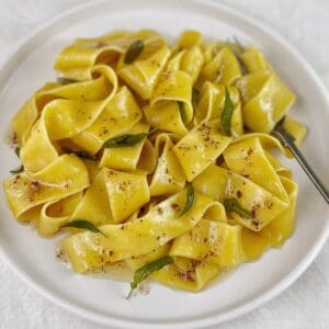 Pasta with butter sauce and crispy sage leaves on a white plate with a fork.