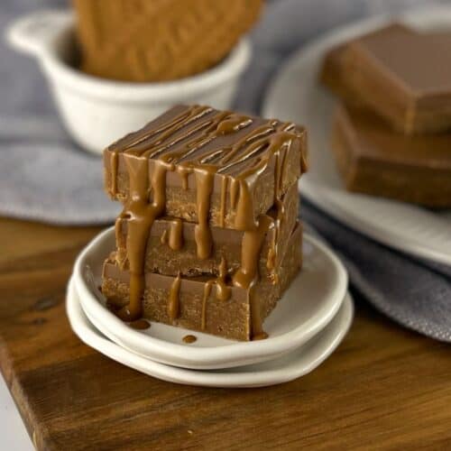 Square pieces of Biscoff slice on a small white plate sitting on a wooden board.