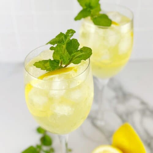 Light yellow coloured drink in a clear glass with mint leaves and a slice of lemon.