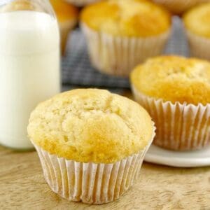 Vanilla muffins sitting on a wooden board with a small bottle of milk.