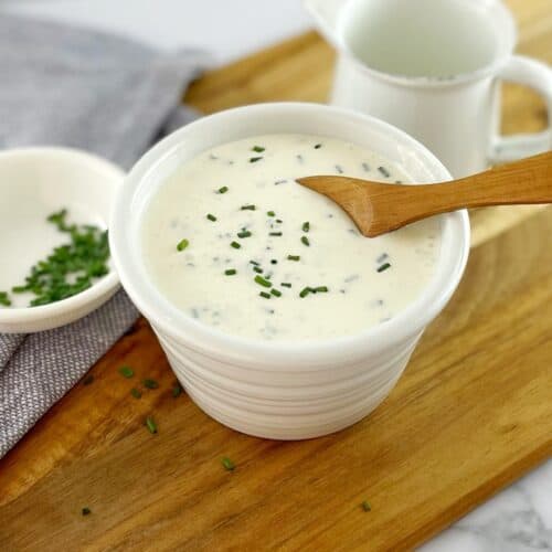 Sour cream sauce in a small white bowl sitting on a wooden board with a spoon.