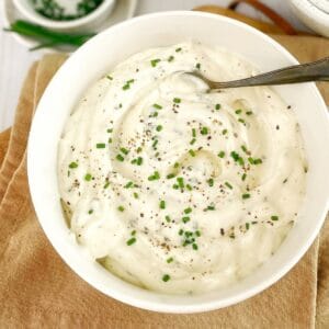 Horseradish mayonnaise sitting in a white bowl sprinkled with chives with a spoon on the side.