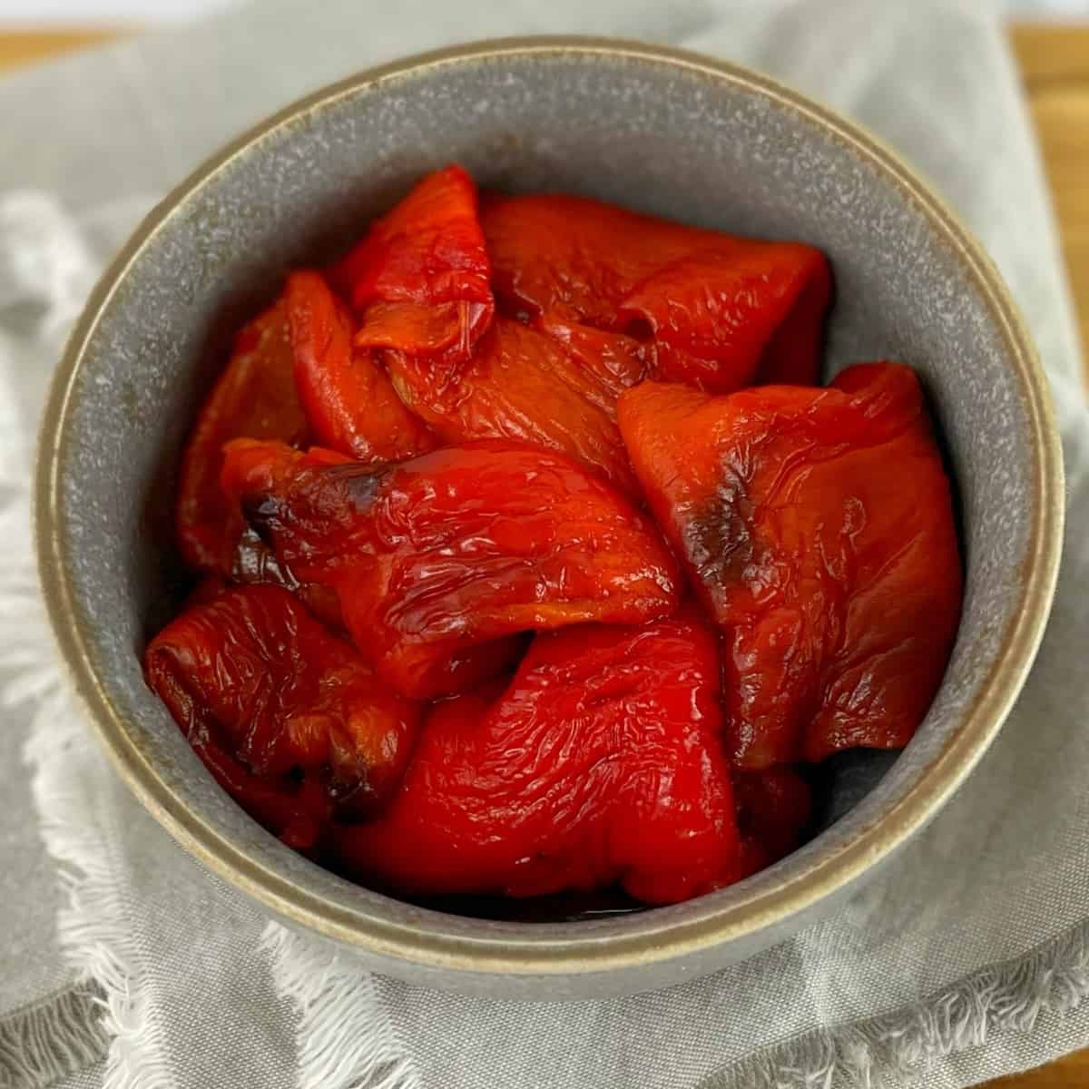 Sliced roasted red capsicums in a gray bowl sitting on a gray tea towel.