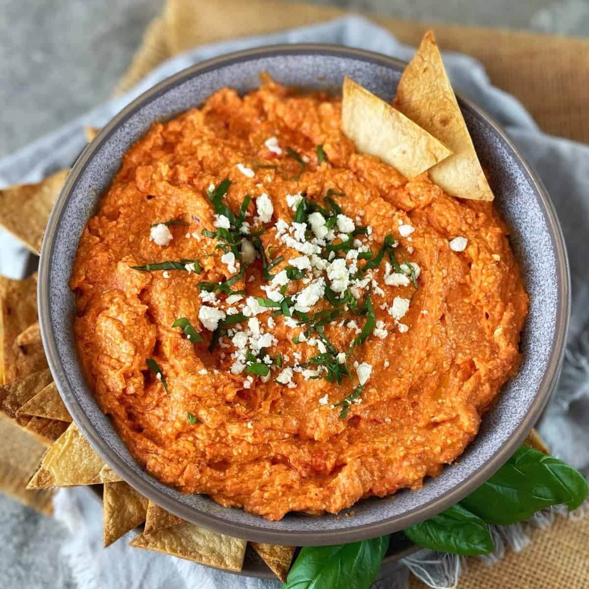 Dip in a gray bowl scattered with basil and feta sitting on a wooden board.