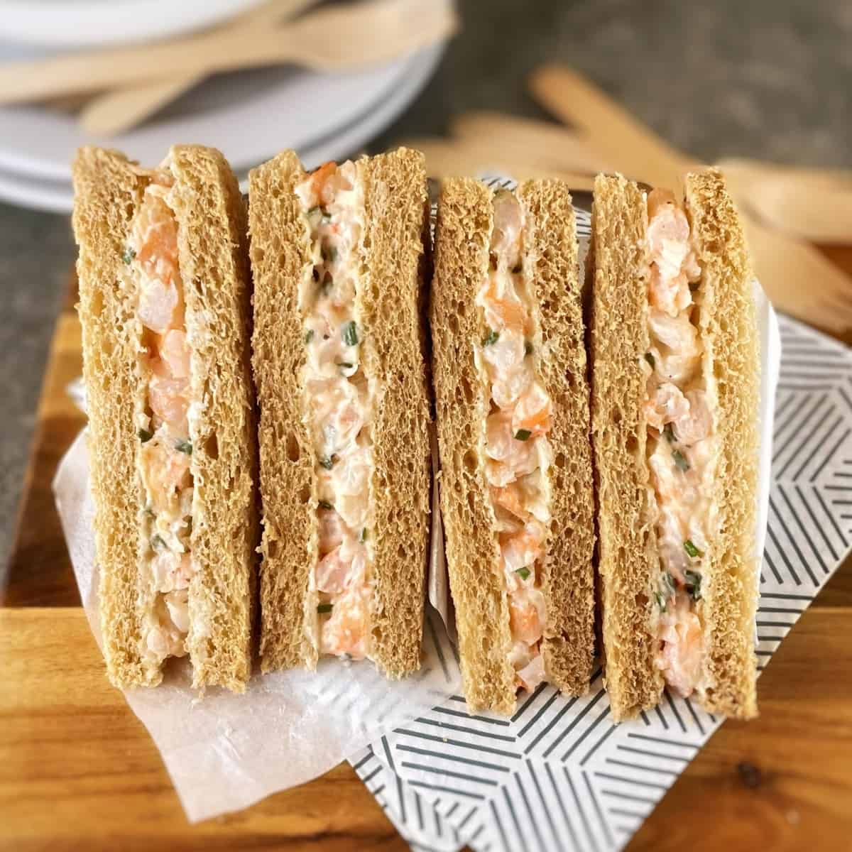 Sandwiches with prawn filling on a wooden board with napkins.