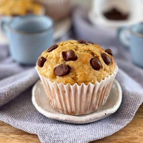Banana muffin with chocolate chips sitting on a wooden board with tea cups.