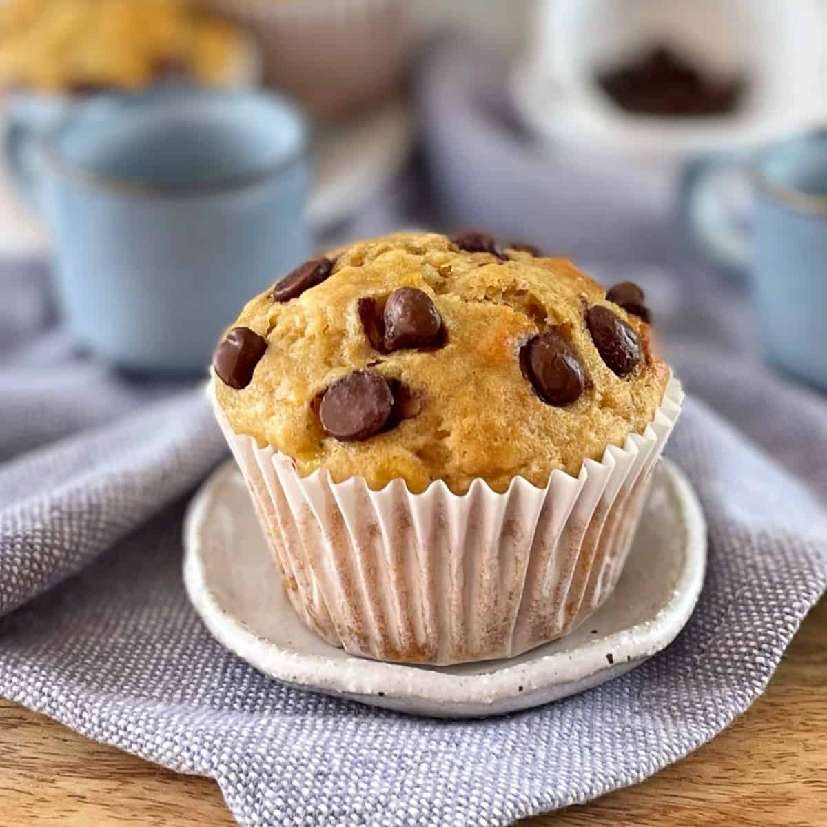 Banana muffin with chocolate chips sitting on a wooden board with tea cups in the background.