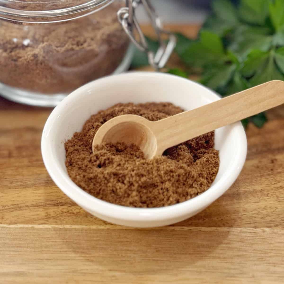 Ground spice mix sitting in a white bowl on a wooden board.