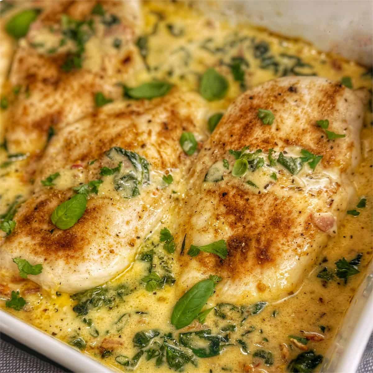 Chicken breasts with a Tuscan cream sauce in a white baking dish.