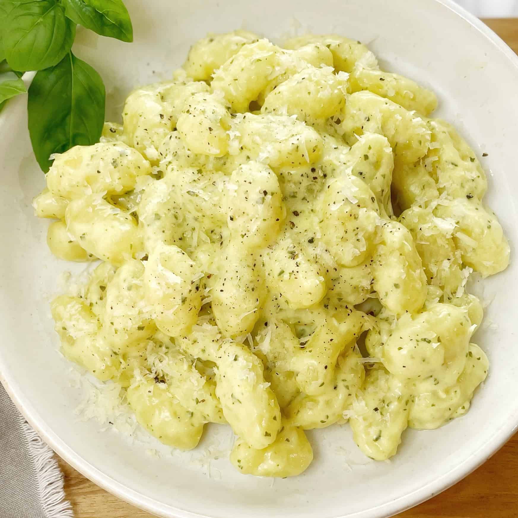 Gnocchi with pesto sauce in a white bowl sitting on a wooden board.