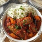 Slow cooker sausage casserole in a white bowl with rice.