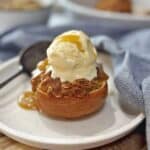 Half a baked apple stuffed with oats sitting on a white plate with a spoon.
