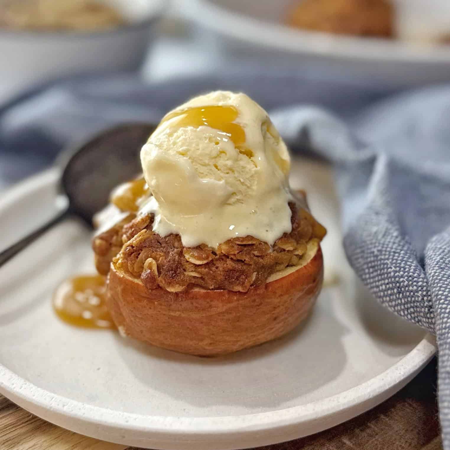 Half a baked apple stuffed with oats sitting on a white plate with a spoon.