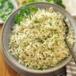 Rice with herbs in a grey bowl with a spoon on wooden board.