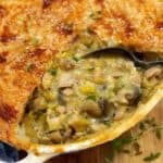 Chicken pie in a white dish on a wooden board with a spoon.