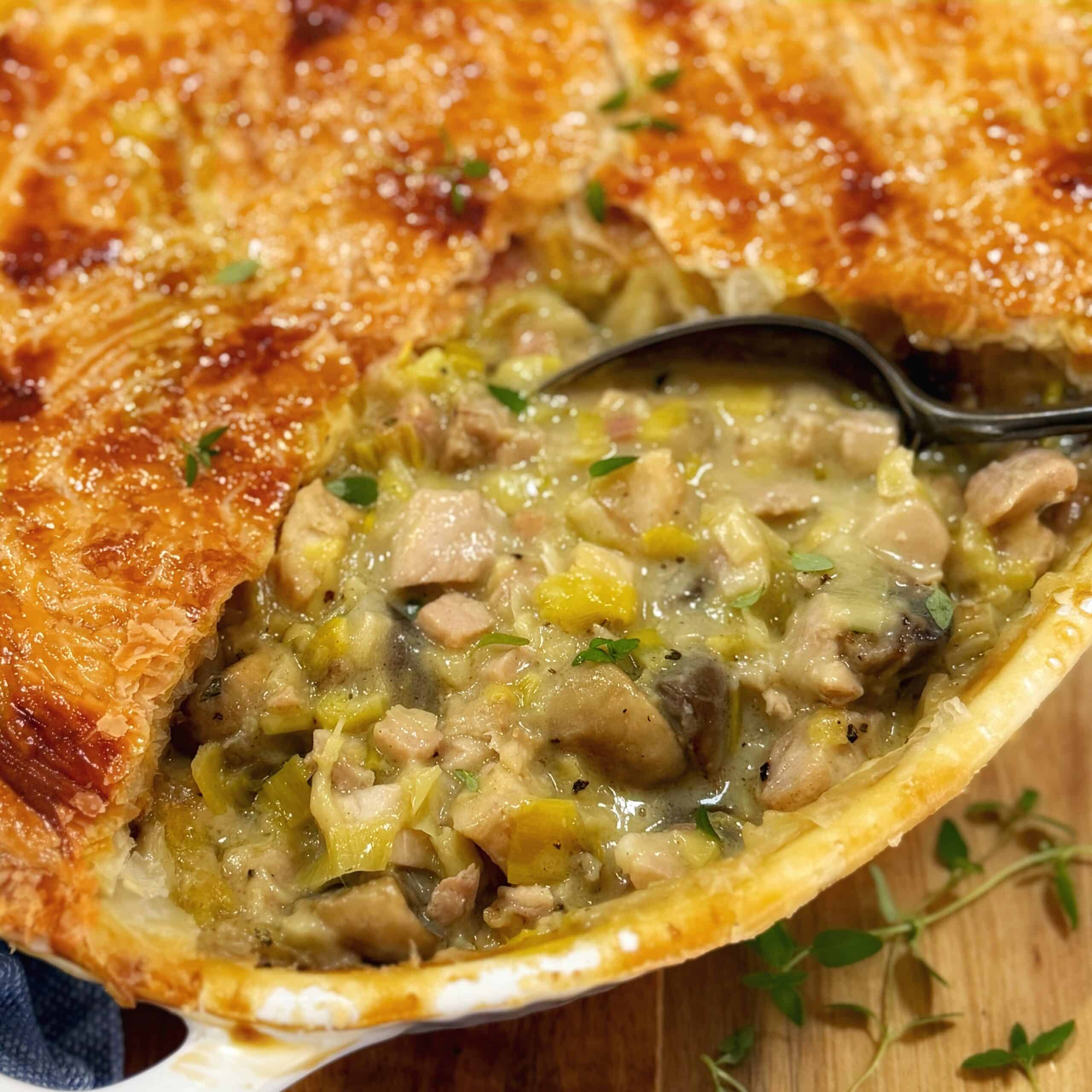 Chicken pie in a white dish on a wooden board with a spoon.
